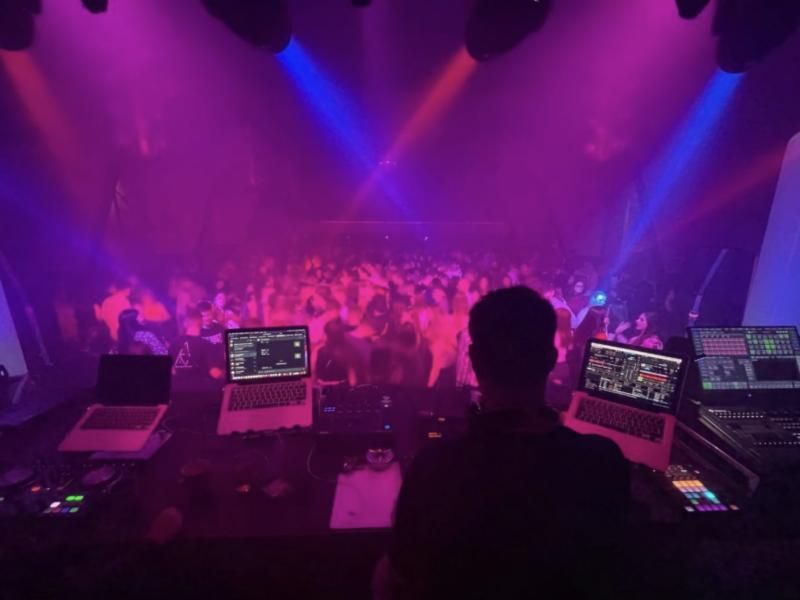 Blick vom DJ-Pult über eine volle Tanzfläche in Magenta-Licht